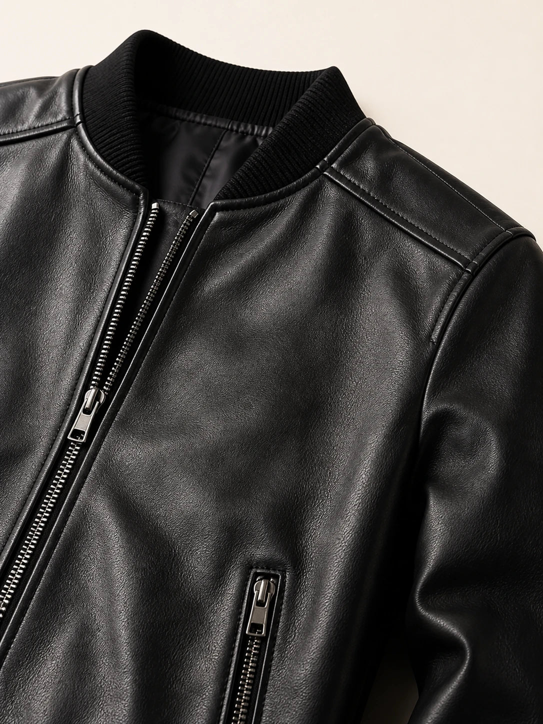 Close-up of the ribbed knit collar, metal zip and welt pocket on the black bomber